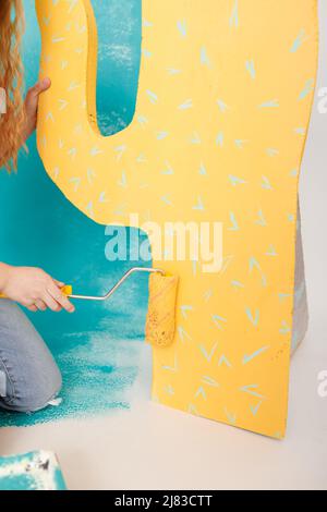 adorable little girl is doing repairs in the apartment fun paints the wall. Portrait of a beautiful smiling child with a paint roller and big paper ca Stock Photo