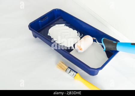Painter's utensils. Roller, brush and tray with white paint in interior work area. Copy space. Stock Photo