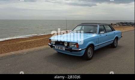 Classic Light Blue Ford Cortina Mk4 on seafront promenade beach and sea in background.