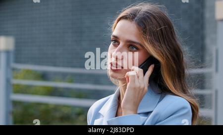 Serious young successful lady business woman girl in blue suit stands on balcony talking mobile phone. Female consultant speaks with smartphone. Buyer Stock Photo