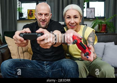 Modern mature Caucasian man and woman in love spending time at home having fun playing video games Stock Photo