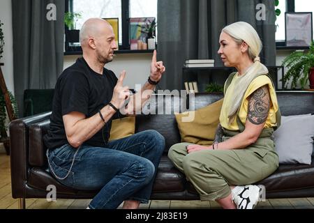 Side view of handsome mature man telling something to his tattooed girlfriend using sign language Stock Photo