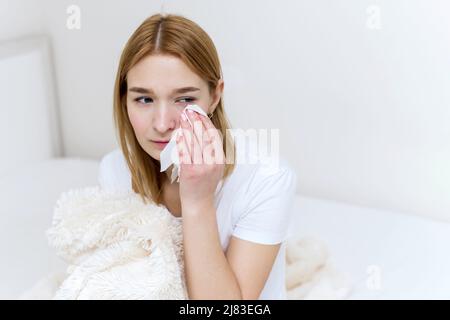 Unhappy depressed caucasian woman crying and wiping away her tears with a paper napkin, suffering from grief in the family. The woman is crying at hom Stock Photo