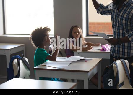 African american elementary schoolboy looking at african american young male teacher in classroom Stock Photo