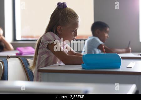 Multiracial elementary school students studying at desk in classroom Stock Photo