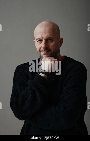 Vertical medium studio portrait of confident mature Caucasian man wearing black sweater looking at camera, gray background Stock Photo