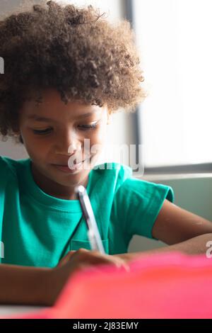 Close-up of smiling african american elementary schoolboy holding pen while sitting at desk in class Stock Photo