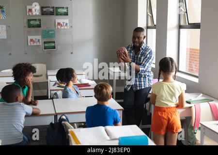 Multiracial elementary students looking at african american young male teacher showing brain model Stock Photo