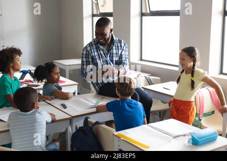 Happy multiracial elementary students looking at multiracial young male teacher showing brain model Stock Photo