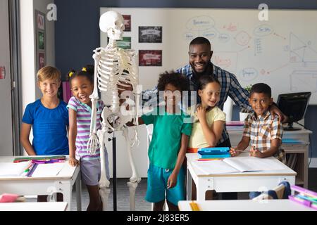 Portrait of smiling multiracial students and african american young male teacher with skeleton Stock Photo