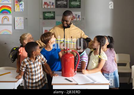 Multiracial elementary students looking african american young male teacher in firefighter uniform Stock Photo