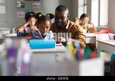 African american young male teacher teaching african american elementary girl on wheelchair in class Stock Photo