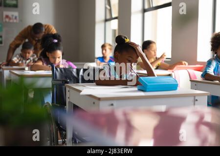 Multiracial elementary school students studying at desk in classroom Stock Photo