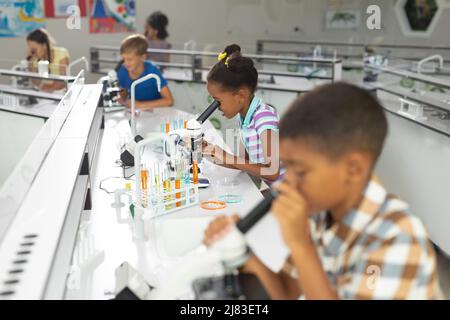 Multiracial elementary students using microscope during science practical in laboratory Stock Photo