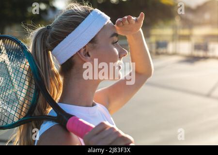 Side view of young caucasian female tennis player shielding eyes while looking away with racket Stock Photo