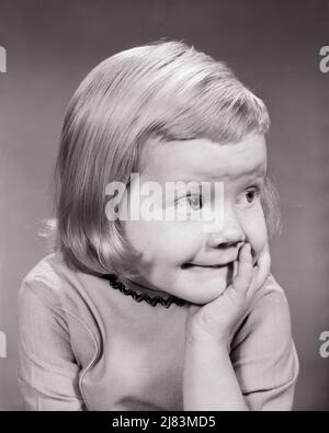 1960s BLONDE GIRL LOOKING OFF TO SIDE MAKING A FUNNY FACE HAND TO HER CHEEK - j1664 HAR001 HARS LIFESTYLE SATISFACTION FEMALES STUDIO SHOT COPY SPACE PENSIVE THOUGHTFUL GESTURING EXPRESSIONS B&W WIDE WONDER HUMOROUS HAPPINESS HEAD AND SHOULDERS CHEERFUL DISCOVERY REFLECTIVE THINK COMICAL GESTURES HESITANT REFLECTING SMILES UNSURE PONDER PONDERING CONSIDER LOST IN THOUGHT COMEDY JOYFUL SHY ASKANCE MAYBE WIDE-EYED DOUBTFUL GROWTH JUVENILES SKEPTICAL BLACK AND WHITE CAUCASIAN ETHNICITY CONSIDERING DUBIOUS HAR001 OLD FASHIONED SUSPICIOUS UNCERTAIN Stock Photo