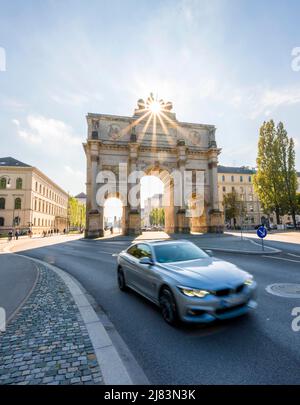 Sun star, Siegestor, Car drives along Leopoldstrasse, Neoclassical architecture, Bavaria, Munich Stock Photo