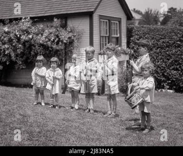 1920s GROUP OF BOYS AND GIRLS IN BACKYARD PLAYING AT BEING SOLDIERS AT ATTENTION WITH TOY GUNS RAKES AND STICKS AND A DRUMMER - j735 HAR001 HARS PERSONS MALES RISK SIBLINGS SISTERS B&W ADVENTURE DRILLING AND ATTENTION SEVEN FORMATION SIBLING UNIFORMS 7 DRUMMER FRIENDLY STICKS STYLISH BB GUN FIREARM FIREARMS JUVENILES PRE-TEEN PRE-TEEN BOY PRESENT ARMS BLACK AND WHITE CAUCASIAN ETHNICITY HAR001 MILITIA OLD FASHIONED RAKES Stock Photo