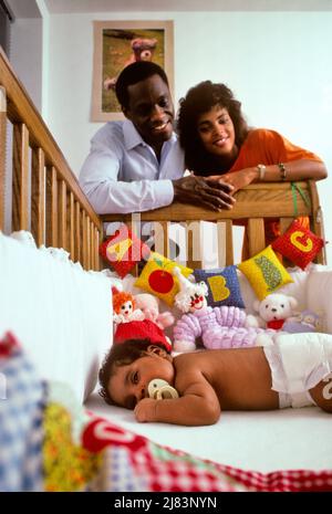 1980s AFRICAN-AMERICAN PARENTS MOM AND DAD LOOKING DOWN ON THEIR SLEEPY BABY BOY IN HIS CRIB LYING ON HIS STOMACH WITH PACIFIER - kb26657 NET002 HARS INDOORS NOSTALGIC CLOWN PAIR SUBURBAN BEAR URBAN COLOR MOTHERS OLD TIME ASLEEP FUTURE NOSTALGIA OLD FASHION 1 JUVENILE INFANT SONS PLEASED FAMILIES JOY LIFESTYLE SATISFACTION PARENTING FEMALES MARRIED SPOUSE HUSBANDS HOME LIFE COPY SPACE LADIES PERSONS INSPIRATION CARING MALES DIAPER CRIB FATHERS PARTNER DREAMS HAPPINESS SLEEPY HEAD AND SHOULDERS CHEERFUL HIS STOMACH TEDDY BEAR AFRICAN-AMERICANS AFRICAN-AMERICAN AND PACIFIER DADS LOW ANGLE Stock Photo