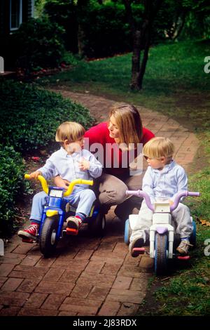 1990s WOMAN MOTHER WITH TWO BOYS SONS RIDING ON TRICYCLES PLAYING OUTSIDE ON SUBURBAN BRICK WALKWAY - kj13382 NET002 HARS COLOR MOTHERS OLD TIME NOSTALGIA BROTHER OLD FASHION 1 JUVENILE STYLE BLOND STRONG SONS FAMILIES JOY LIFESTYLE PARENTING BRICK FEMALES BROTHERS GROWNUP HOME LIFE COPY SPACE PEOPLE CHILDREN FRIENDSHIP HALF-LENGTH LADIES PERSONS CARING MALES SIBLINGS TRANSPORTATION HOMEMAKER HOMEMAKERS HIGH ANGLE ADVENTURE LEISURE AND EXCITEMENT AUTHORITY SIBLING BABY BOY PERSONAL ATTACHMENT WALKWAY AFFECTION EMOTION FISHER PRICE GROWTH JUVENILES MID-ADULT MID-ADULT WOMAN MOMS TOGETHERNESS Stock Photo