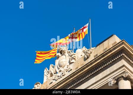 Flags of Spain, city of Barcelona and the autonomous community of Catalonia waving in the wind against part of ancient building and clear blue sky bac Stock Photo