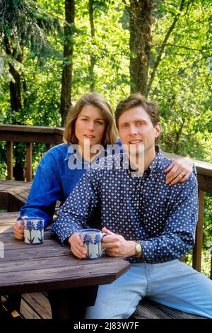 1990s PORTRAIT COUPLE DRINKING COFFEE RELAXING ON PORCH HER HAND WITH WEDDING RING RESTING ON HIS SHOULDER LOOKING AT CAMERA - ks35808 NET002 HARS OLD TIME NOSTALGIA OLD FASHION COTTON RELAXING LIFESTYLE ARCHITECTURE FEMALES HOUSES MARRIED RELAX RURAL SPOUSE HUSBANDS GROWNUP HEALTHINESS HOME LIFE COPY SPACE FRIENDSHIP HALF-LENGTH LADIES PERSONS RESIDENTIAL MALES BUILDINGS DENIM MORNING PARTNER RESTING EYE CONTACT HAPPINESS HIS LEISURE DETAILS PORCHES HOMES STORIES CONNECTION RESIDENCE ARCHITECTURE DETAIL ARCHITECTURE DETAILS BLUE JEANS INFORMAL MID-ADULT MID-ADULT MAN MID-ADULT WOMAN Stock Photo