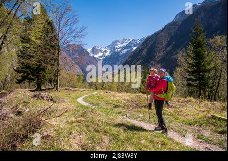 Mother holding his daughter in embrace while walking on forest meadow. Stock Photo