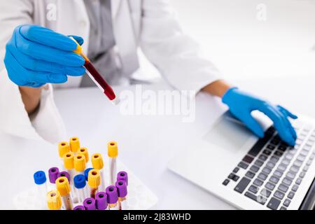 Midsection of african american mid adult woman wearing glove holding test tube and using laptop Stock Photo