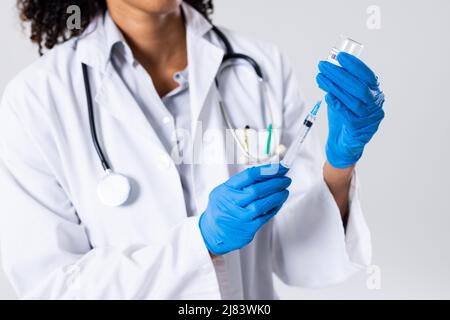 Midsection of african american mid adult female doctor wearing gloves holding syringe and vial Stock Photo