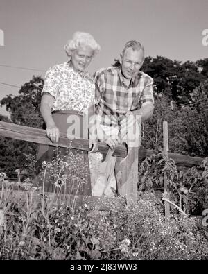 1960s SENIOR COUPLE WOMAN WITH MAN POINTING LOOKING OVER FENCE INTO GARDEN AT FLOWERS AND TOMATO PLANTS - s14958 HAR001 HARS COMMUNICATION TEAMWORK TOMATO LIFESTYLE SATISFACTION ELDER FEMALES MARRIED SPOUSE HUSBANDS HEALTHINESS HOME LIFE NATURE COPY SPACE FRIENDSHIP HALF-LENGTH LADIES PERSONS MALES PLANTS RETIREMENT SENIOR MAN SENIOR ADULT B&W PARTNER SENIOR WOMAN GARDENER RETIREE HAPPINESS OLD AGE OLDSTERS OLDSTER AND LOW ANGLE RECREATION ELDERS CONNECTION GARDENS STYLISH GARDENERS COOPERATION GROWTH SPADE TOGETHERNESS WIVES BLACK AND WHITE CAUCASIAN ETHNICITY HAR001 OLD FASHIONED Stock Photo