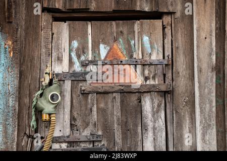 An old gas mask and a dangerous sign with a painted skull hang on the door, gas attack in Ukraine during the war, protective mask, ecology, chemical a Stock Photo