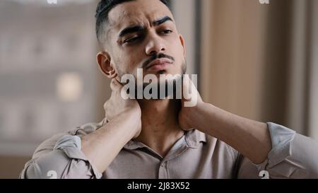Tired hispanic exhausted man businessman employee suffering from muscles tension having painful neck due to working overtime in office overwhelmed Stock Photo