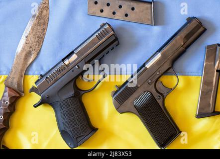 Pistols, knives, magazines for bullets lie on the flag of Ukraine, the war in Ukraine, weapons for soldiers 2022 Stock Photo