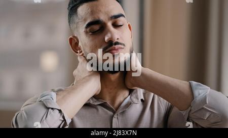 Tired hispanic exhausted man businessman employee suffering from muscles tension having painful neck due to working overtime in office overwhelmed Stock Photo