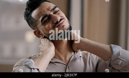 Tired hispanic exhausted man businessman employee suffering from muscles tension having painful neck due to working overtime in office overwhelmed Stock Photo