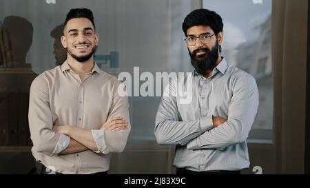 Two male friends multiracial diverse colleagues business partners hispanic man arabian bearded guy standing in office posing with crossed arms nodding Stock Photo