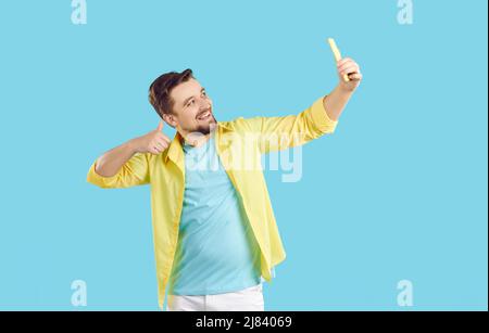 Happy young man smiling, showing thumbs up and taking selfie on his mobile phone Stock Photo