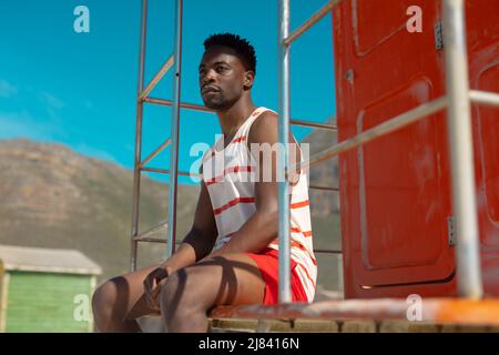 Thoughtful african american young man looking away while sitting on lifeguard hut against clear sky Stock Photo