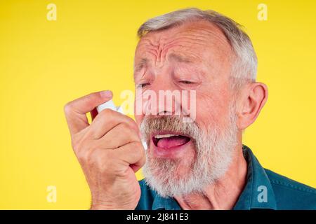 Senior man using an asthma inhaler in studio yellow background Stock Photo
