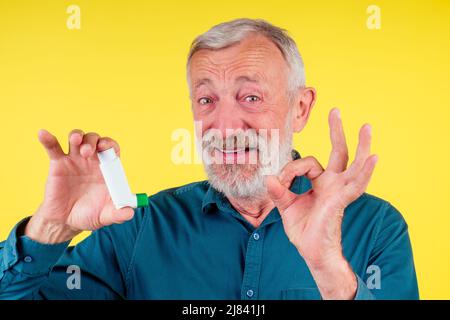 Senior man using an asthma inhaler in studio yellow background Stock Photo