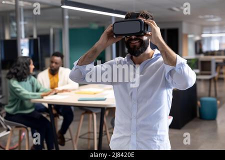 Smiling caucasian businessman wearing virtual reality simulator at modern workplace Stock Photo