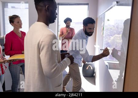 Caucasian businessman writing strategy on whiteboard during meeting with multiracial colleagues Stock Photo