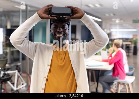 Portrait of happy african american businessman wearing virtual reality simulator at workplace Stock Photo