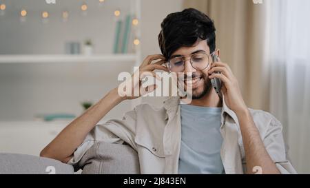 Bearded man with glasses sitting on sofa at home talking on mobile phone call chatting with friends girlfriend friendly remote conversation Stock Photo