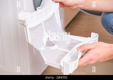 A man takes a lint filter out of the dryer and cleans it from dust, lint, hair, wool. Stock Photo