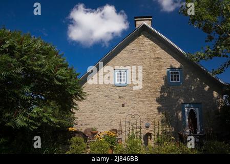 Brown wicker chairs on patio next to old circa 1850 Canadiana cottage style fieldstone home in summer. Stock Photo