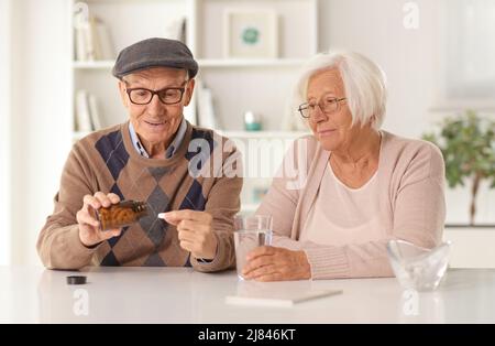 Elderly couple sitting at a table at home and taking vitamin pills Stock Photo