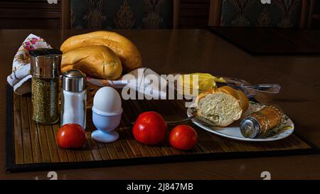 A soft-boiled egg for breakfast with fresh rolls, butter, a cup of tea and a bunch of beautiful tomatoes. The photo can be used on canvas and poster. Stock Photo