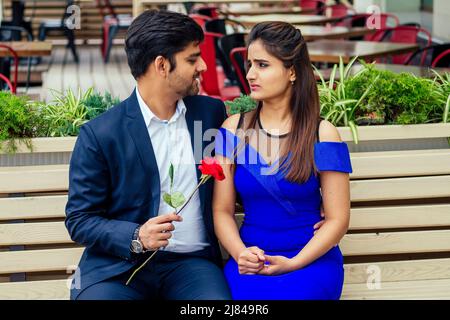 long haired brunette indian woman in blue dress with her handsome boyfriend having dating .man giving rose to his girlfriend in summer downtown street Stock Photo