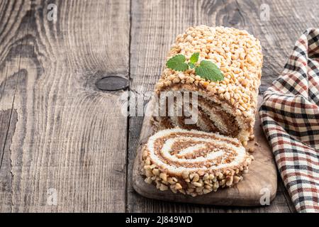 Sponge  cake roll covered with nuts on wooden table Stock Photo